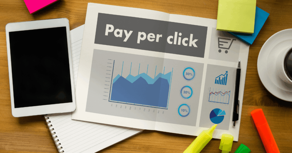 Mesa com tablet, caderno e gráfico de desempenho com a palavra pay per click, representando análise e estratégias de campanhas PPC